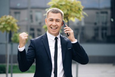 Akıllı telefondan iyi haberler okuyan heyecanlı adamın portresi. Başarılı iş adamı dışarıda cep telefonuyla zaferi kutluyor. Şaşkın adam dışarıda cep telefonu gibi duruyor.