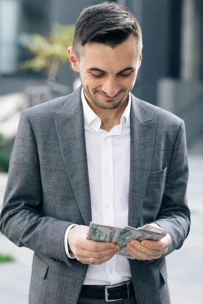 Knappe rijke man dragen stijlvolle pak tellen geld staande in de straat in de buurt van kantoorgebouw — Stockfoto