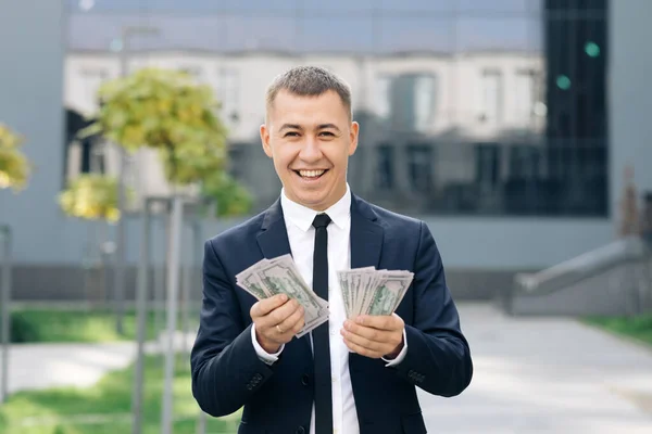 Succesvolle zakenman die geld telt. Glimlachende man geniet van een goede deal in de buurt van modern kantoor. De man verdiende makkelijk geld. Een rijke man in een stijlvol pak met een zonnebril die geld telt.. — Stockfoto