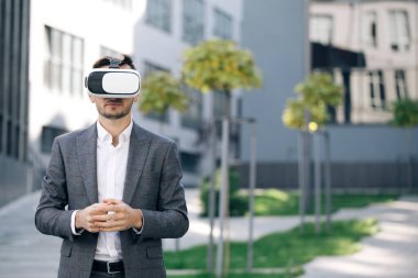 Sanal gerçeklik kulaklığı takan yakışıklı bir adam. Artırılmış Gerçeklik. İşadamı ofis binasının yakınındaki modern 3D VR gözlüklerini kullanarak bir şeye dokunuyor. Bu yeni teknoloji yeni 3D boyutlar sunuyor