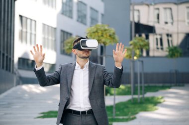 Artırılmış Gerçeklik. İşadamı ofis binasının yakınındaki modern 3D VR gözlüklerini kullanarak bir şeye dokunuyor. Bu yeni teknoloji yeni üç boyutlu boyutlar sunuyor. Sanal gerçeklik kulaklığı takan yakışıklı adam.