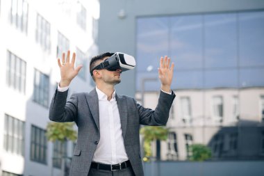 Sanal gerçeklik kulaklığı takan yakışıklı bir adam. Artırılmış Gerçeklik. İşadamı ofis binasının yakınındaki modern 3D VR gözlüklerini kullanarak bir şeye dokunuyor. Bu yeni teknoloji yeni 3D boyutlar sunuyor