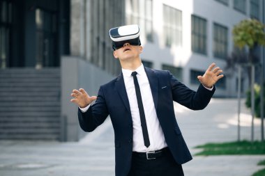 Sanal gerçeklik kulaklığı takan yakışıklı bir adam. Artırılmış Gerçeklik. İşadamı ofis binasının yakınındaki modern 3D VR gözlüklerini kullanarak bir şeye dokunuyor. Bu yeni teknoloji yeni 3D boyutlar sunuyor