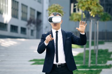 Sanal gerçeklik kulaklığı takan yakışıklı bir adam. Artırılmış Gerçeklik. İşadamı ofis binasının yakınındaki modern 3D VR gözlüklerini kullanarak bir şeye dokunuyor. Bu yeni teknoloji yeni 3D boyutlar sunuyor