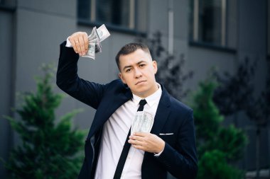 Man shows money and celebrating success, victory while looking to camera. Outdoors. Amazed happy excited businessman with money - U.S. currency dollars banknotes clipart