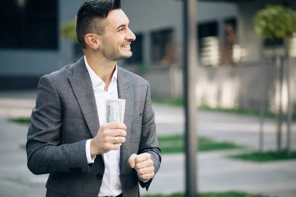 Felice uomo ricco di successo tiene dollari all'aperto. Ritratto di uomo d'affari soddisfatto detiene denaro. Stile di vita, ricchezza, gioia, successo — Foto Stock