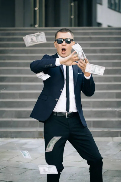 Jeune homme d'affaires heureux disperser les dollars dans la rue près du centre de bureau. pluie d'argent, chute de dollars. une entreprise prospère. drôle homme jette de l'argent — Photo
