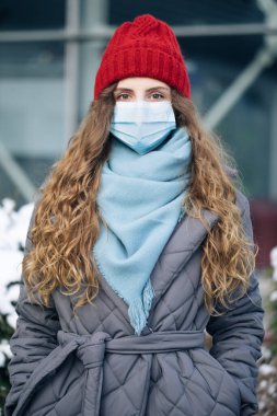 Şehir sokaklarında gün boyunca kıvırcık saçlı bir kadının portresi. Hava kirliliğine karşı maske takıyor ve Coronavirus Covid19 kameraya bakıyor.