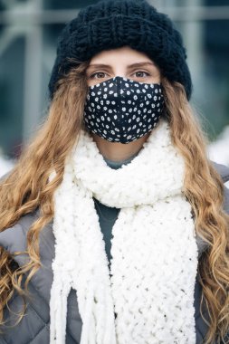 Gün boyunca şehir sokaklarında kahverengi kıvırcık saçlı bir kadının portresi. Hava kirliliğine karşı maske takıyor ve Coronavirus Covid19 kameraya bakıyor..