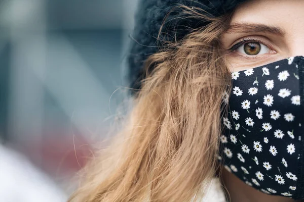 Gekrulde vrouw draagt een beschermend masker om besmetting met het coronavirus te voorkomen. Gezondheid en veiligheid Close-up van vrouwelijke helft gezicht op straat. Portret van een blanke vrouw die naar de camera kijkt. — Stockfoto