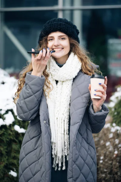 Portrait of Curly haired Woman with phone using the voice recognition ai audio message on the phone, audio message ai speech helper. Vacation winter outdoor