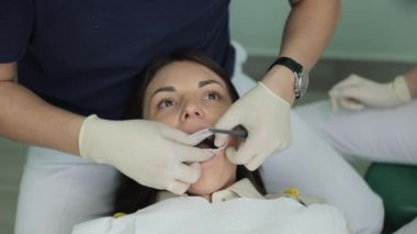 Profesyonel dişçi, hastaların dişleri ve ağızları açık eldivenlerle çalışıyor. Oral yardım kavramı. Diş hekimi tıbbi aletlerle dişleri inceliyor. Diş hijyeni prosedürü