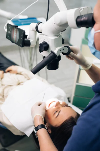 Close-up de um dentista usando microscópio. Microscópio de equipamento moderno em consultório odontológico. Médico dentista usando microscópio dentário em consultório odontológico moderno. O endodontista está tratando canais — Fotografia de Stock