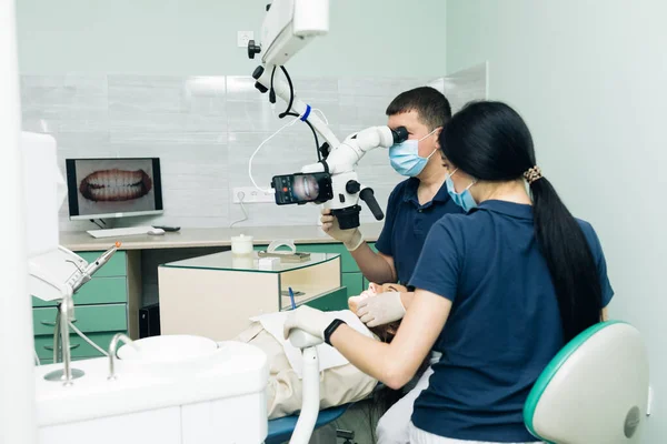 Conceito de Estomatologia Médica. Médico fazendo exame de dentes pesquisa usando microscópio em odontologia. Dentista está tratando paciente em consultório odontológico moderno — Fotografia de Stock