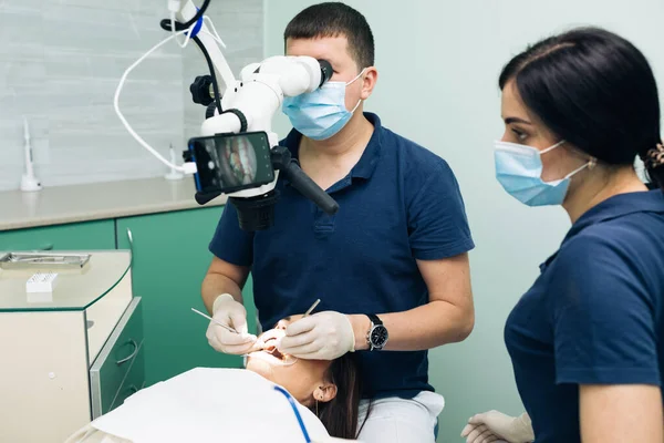 Estomatologista trata dente com ferramentas médicas. Dentista masculino, juntamente com assistente de tratamento de dentes femininos na clínica. Estomatologia. Tratamento. Conceito para odontologia — Fotografia de Stock