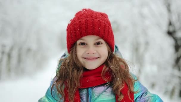Nahaufnahme des glücklichen süßen Mädchens, das in die Kamera blickt und den Hintergrund eines verschneiten Waldes lächelnd betrachtet. Positives Kind. Porträtaufnahme. Draußen. Die Toten des Winters, Kälte, Frost, Schnee — Stockvideo