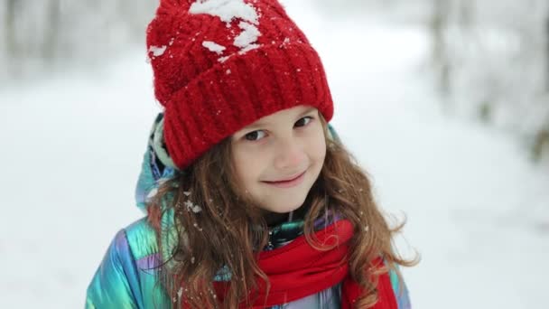 Lustige süße Mädchen lachen draußen im Winter Tag. Hübsches kleines Mädchen mit langen Haaren, roter Mütze und Schal, das zur Winterzeit im weißen verschneiten Park oder Wald steht. — Stockvideo