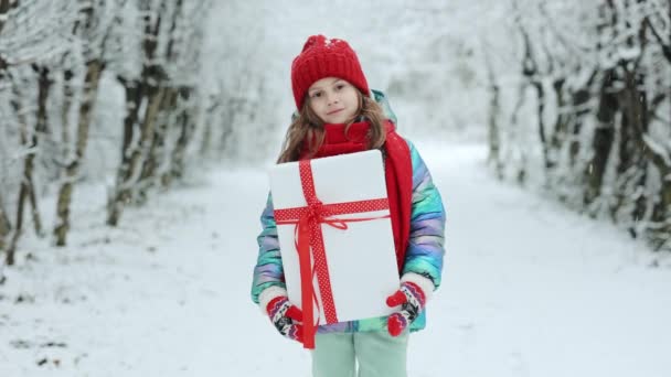 クリスマスの箱の贈り物を持つ少女クリスマスの前夜に屋外で冬に。幸せな小さな白人の女の子の笑顔とクリスマスの日にギフトボックスを保持します。ギフトボックスと驚きの顔を持つ子供 — ストック動画