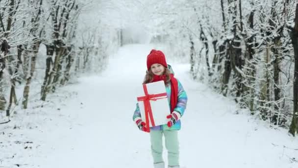 Glückliches Mädchen mit Weihnachtsgeschenk auf einem Winterspaziergang in der Natur. Kleines Mädchen genießt die Ferien. Porträt Kind mit Geschenkbox auf winterlichem Hintergrund — Stockvideo