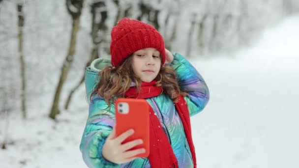 Nettes kleines Mädchen, das ein Selfie im Winterwald macht. Winterreisen mit Kindern. Liebenswert glücklich lächelndes Kind Mädchen genießen Selfie-Kamera mit dem Smartphone aufgenommen — Stockvideo