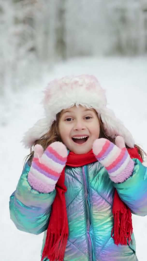 Vídeo vertical Retrato de una linda niña en invierno. Niño feliz en el bosque de invierno. Sorprendido hermosa chica que mira a la cámara y sonríe. — Vídeos de Stock