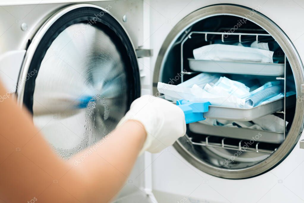 Nurse putting instruments in special craft paper bags into autoclave for processing. Modern laboratory equipment. Tools sterilization, bacterial purification and disinfection in dental clinic