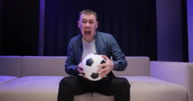 25 'lerin genç, eğlenceli futbolcusu. Takımın favori takımını neşelendirin. Koyu renk oturma odasında kot ceketli, beyaz tişörtlü futbol topu tutun. İnsanların duyguları eğlence yaşam tarzı konseptini besler.