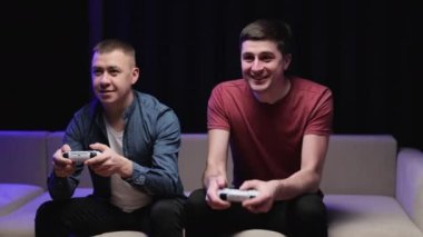 Heyecanlı genç yetişkin erkek oyuncular ellerinde bilgisayar oyunu oynuyorlar arkadaşlar video oyunu kazanıp evde zaferi kutluyorlar..