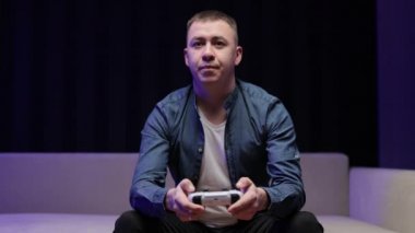 Heyecanlı adamın video oyunu oynayıp joystick kullanmasını ön planda görmek. Yakışıklı adam oturma odasında kanepede otururken tek başına vakit geçiriyor.