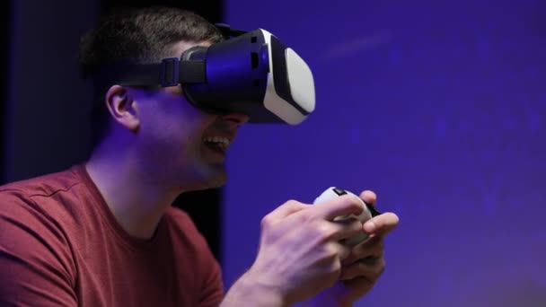 Ελκυστικός καυκάσιος άντρας κρατάει χειριστήριο και φοράει γυαλιά εικονικής πραγματικότητας το Σαββατοκύριακο. Ευτυχία gamer κάνουν ένα διάλειμμα με το παιχνίδι χρησιμοποιώντας τα γυαλιά VR στο σαλόνι — Αρχείο Βίντεο