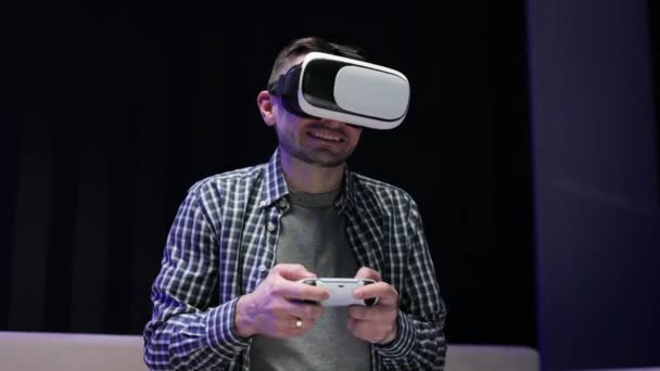Геймер грає в гру, використовуючи окуляри VR вдома. Крупним планом портрет привабливого білоруського чоловіка тримає джойстик і носить окуляри віртуальної реальності шолом гарнітура на дивані вдома . — стокове відео