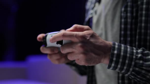 Close-up of the man holding a white joystick next gen console and playing a video game on TV. Males hands holding joystick, playing video game and having fun — Stock Video