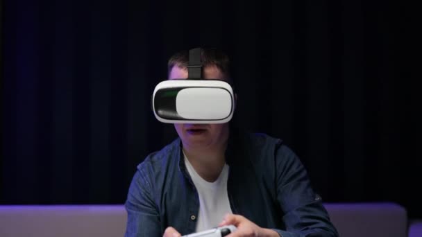 Bărbatul atractiv ține joystick și poartă ochelari de realitate virtuală casca cu cască pe canapea acasă. Fericire gamer joc folosind ochelari VR la domiciliu . — Videoclip de stoc