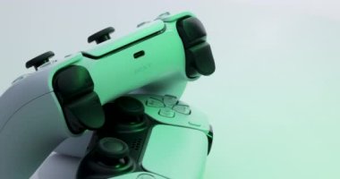 NEW YORK - 3 Mart 2021: Sony Playstation 5 denetleyici. Kamera yeşil ışıkta TV oyun kutusundan çıkan beyaz kumandanın etrafında dönüyor. İki beyaz oyun denetleyicisi Sony Playstation 5.