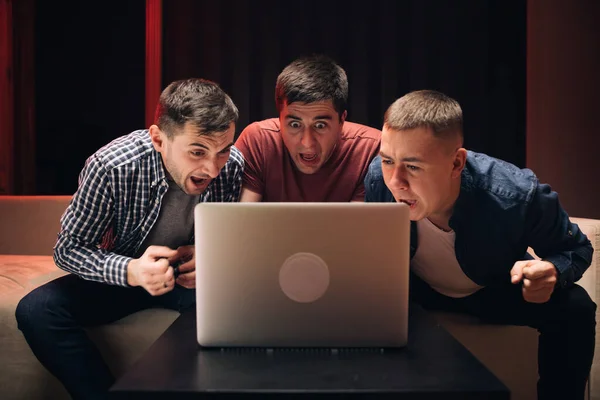 Male friends watching online football game match at laptop. Men watching football in streaming on laptop. Men fans buddies supporters cheering celebrating victory goal score support winning team