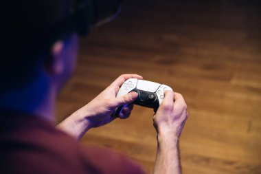 Geniş ekran TV 'nin önünde oyun konsolunda video oyunu oynayan erkek elleri. Adam Play Station 5 çift duyu kontrolörüyle oynuyor. Renkli ışıklar.