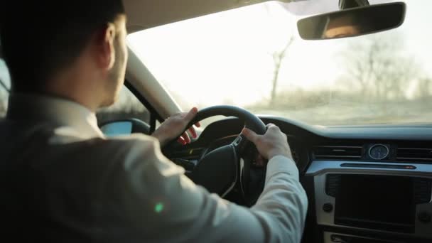 Los conductores de la mano en el volante contra el fondo de la carretera. Disfrutando del cielo al atardecer. La libertad inspira. Vista trasera al joven conduce un coche. Los rayos del sol brillan a través del parabrisas del vehículo. — Vídeos de Stock