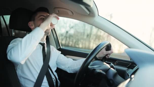 Happy stylishly dressed man drinking coffee in the car. Relaxed business man driving car and drink a coffee in highway. Man driving a car on country road trip in nature with sunset and sun flare — Stock videók