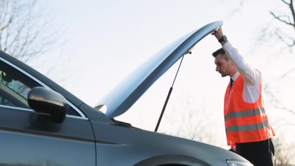 Hombre decepcionado en traje formal abriendo el capó del coche averiado para comprobar el motor. Empresario barbudo llega tarde a la reunión de trabajo debido a problemas en la carretera — Vídeo de stock