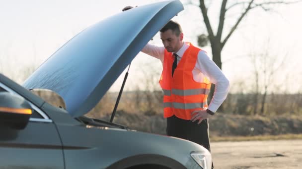 Disappointed man in formal outfit opening bonnet of broke down car to check engine. Sad businessman standing near car opened the hood. Car accident on the road. Emergency stop sign. — Stock Video