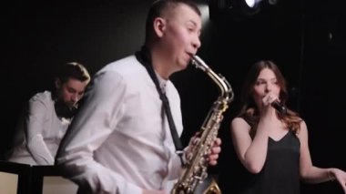 Müzik grubu dansındaki vokalist kız, konserdeki müzisyen sahnesinde dumanla şarkı söylüyor. DJ parti konserinde sahne alacak. Saksafoncu, altın saksafonda çalıyor. Canlı performans