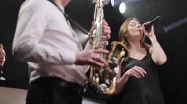 Müzik grubu dansında şarkı söyleyen kız konser müzisyenleri sahnesinde dumanla şarkı söylüyor. DJ parti konserinde sahne alacak. Saksafoncu, altın saksafonda çalıyor. Canlı performans.