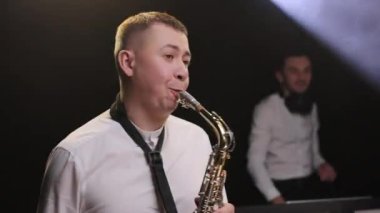 Gece kulübünde saksafoncu, saksafon çalan, dans eden, DJ 'le konser veren enerjik saksafoncu adama yakın çekim. Parti, müzik festivali konseri.