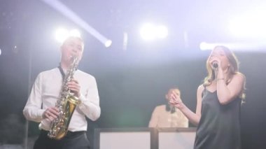 Üç kişilik bir müzik grubu şarkı söylüyor, sahne performansları sergiliyorlar. Şarkıcı kız, saksafoncu saksafoncu, DJ. Dans eden aktörler, bandoda şarkı söyleyen müzisyenler.