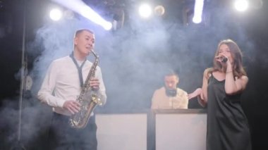 Sahnede şarkıcıyla konser veren müzik grubu. Vokalist kadın müzik grubu, saksafoncu saksafoncu, DJ adam konser müzisyeni sahnesinde ışıklar altında şarkı söylüyor.