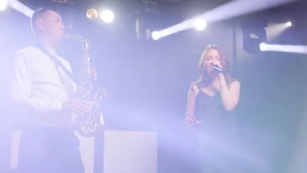Singer vocalist girl, saxophonist sax, dj man forward in dark musician nightclub disco for concert on stage. Light appears and illuminates musical group band. Concert atmosphere — Stock Video