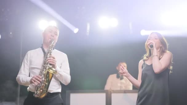 Gruppo musicale composto da tre persone che suonano la canzone, esibendosi sul palco del concerto musicista con luci. Singer vocalist girl, sax sassofonista, dj man. Attori che ballano, cantano Musicista che suona in banda — Video Stock