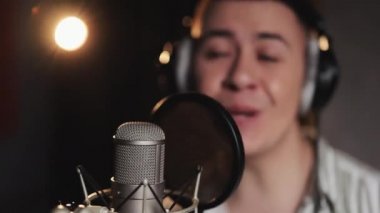 Kulaklık takan, şarkı söyleyen ya da bir kayıt stüdyosunda mikrofona vurup el kol hareketi yapan melez erkek şarkıcının ön görüntüsü. Kayıt stüdyosunda şarkı kaydetme süreci