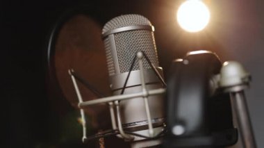 Sahnedeki mikrofonun siyah arka planına yakın plan ışıklandırmalı. Karanlıktaki mikrofonun silueti. Müzik aleti konsepti. Podcast, radyo, röportaj, müzik stüdyosu kaydı