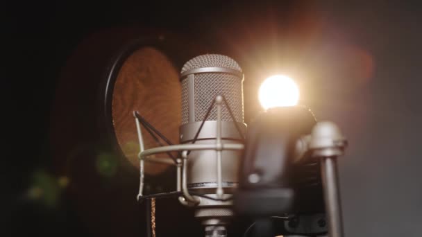Close up Microfone profissional e fones de ouvido no estúdio de gravação de som. Microfone no palco contra um fundo preto com iluminação. Conceito de gravação — Vídeo de Stock